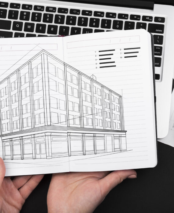 "Architectural sketch of modern commercial building with laptop keyboard and coffee cup on black desk"