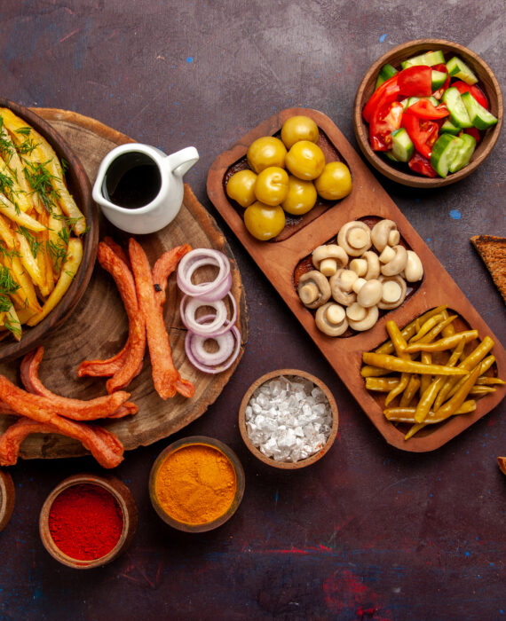 "Rustic spread of fried potatoes with fresh dill, sausages, vegetables, spices and rye bread on dark background"