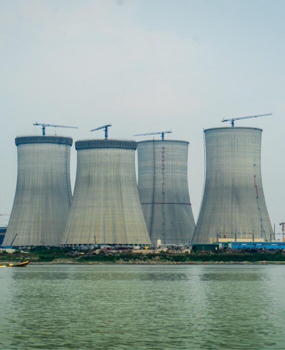 "Rooppur Nuclear Power Plant cooling towers under construction along riverbank in Bangladesh with construction cranes visible"